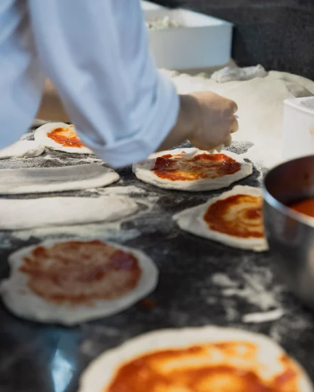 Pizzaiolo che stende l'impasto a mano sul bancone infarinato